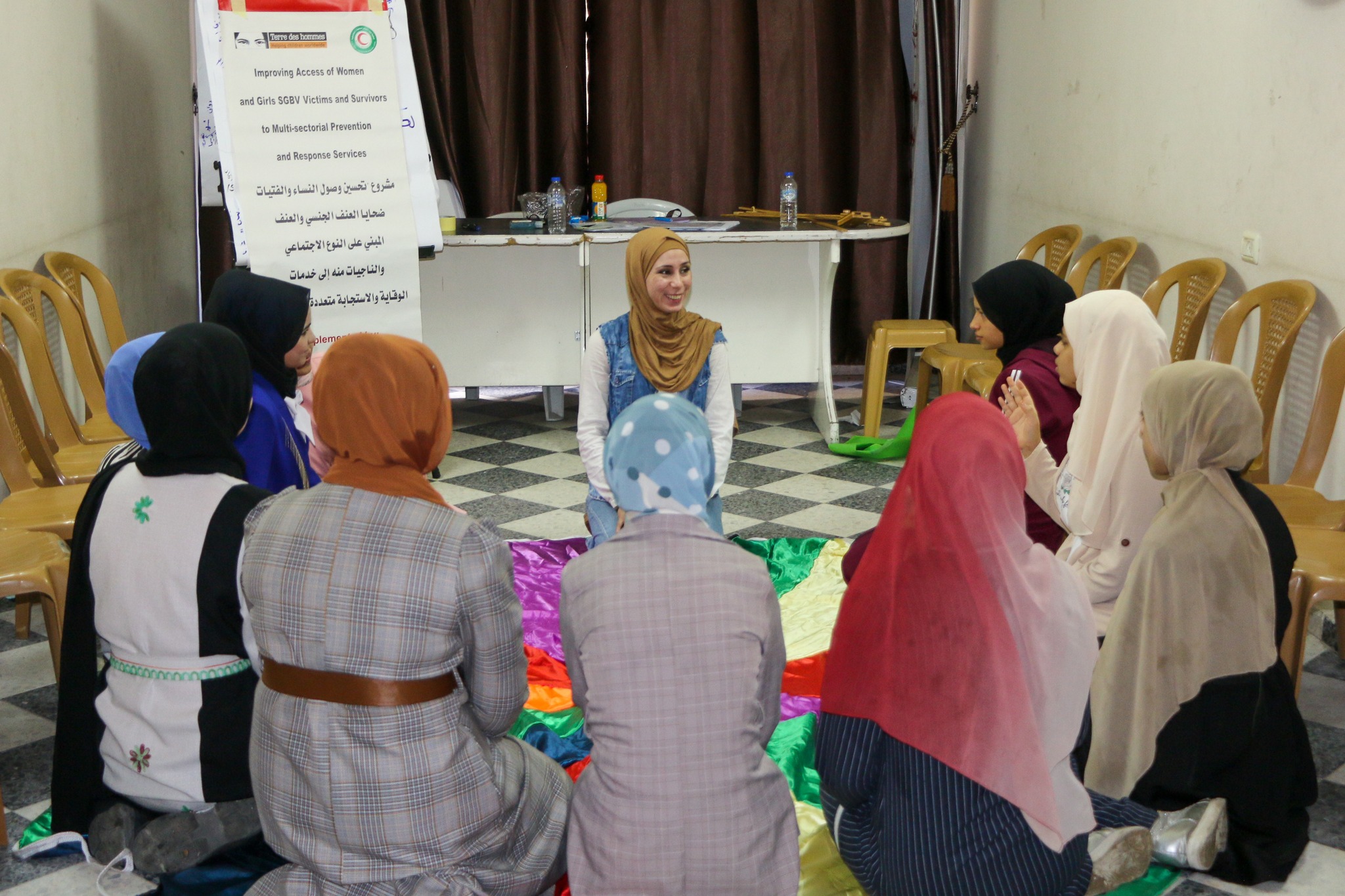 girls sitting on the floor in a circle with a colourful canvas in front of them